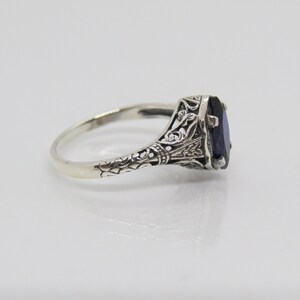 May include: A silver ring with an oval-shaped blue gemstone set in a filigree design.