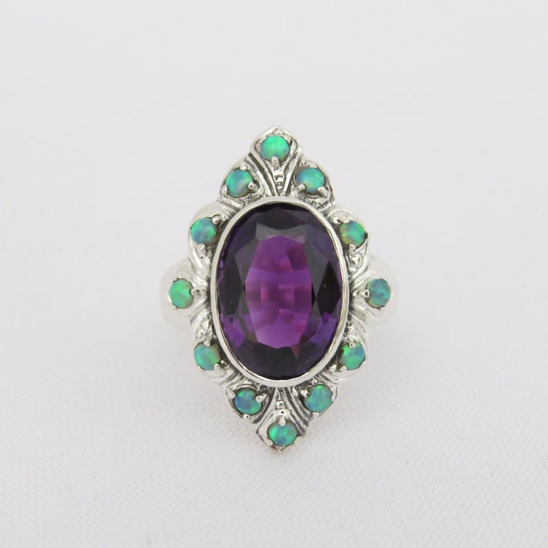 May include: A silver ring with a large oval amethyst gemstone surrounded by smaller green opal gemstones.