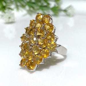 May include: A silver ring with a cluster of yellow citrine gemstones. The stones are set in a graduated pattern, creating a unique and eye-catching design.