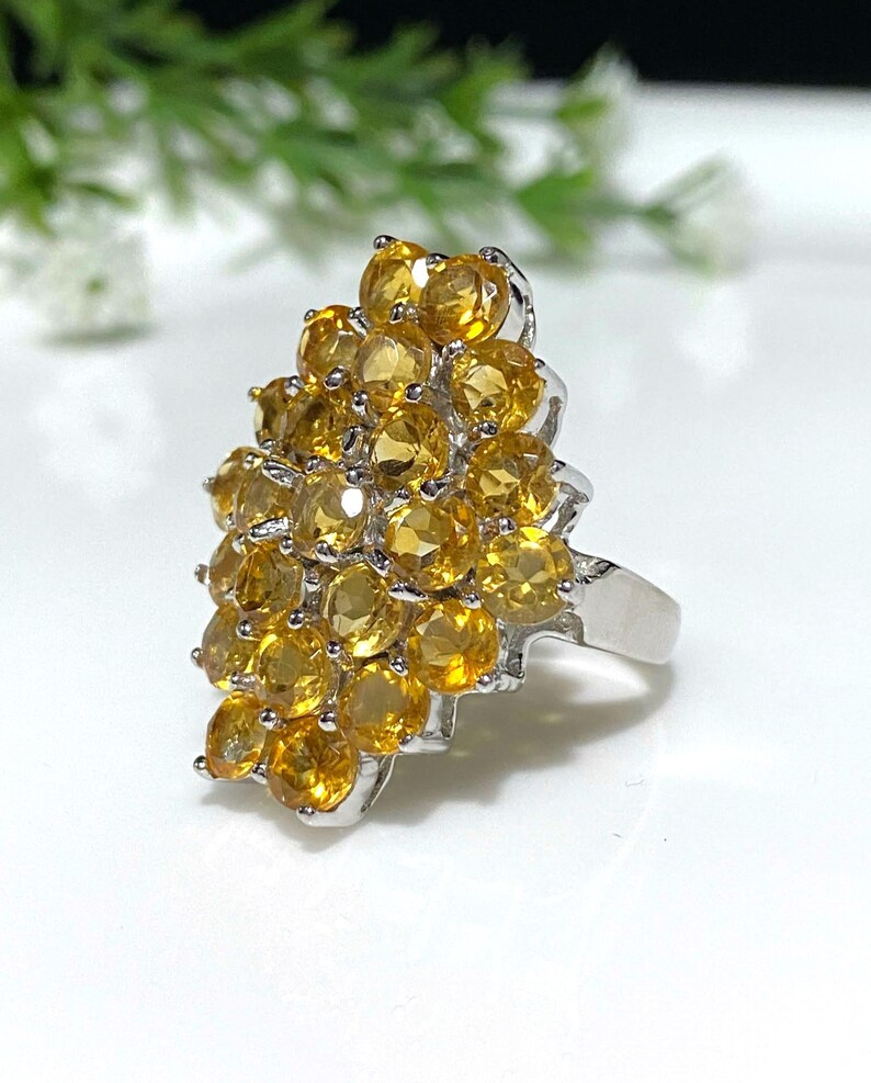 May include: A silver ring with a cluster of yellow citrine gemstones. The stones are set in a graduated pattern, creating a unique and eye-catching design.