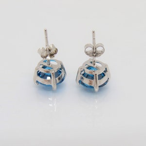 Puede incluir: Un par de pendientes de plata con una piedra preciosa azul en cada uno. Las piedras preciosas son redondas y tienen un dise&ntilde;o facetado.