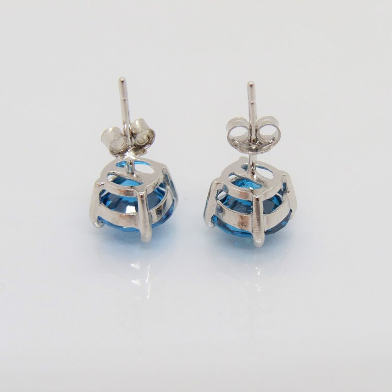 Puede incluir: Un par de pendientes de plata con una piedra preciosa azul en cada uno. Las piedras preciosas son redondas y tienen un dise&ntilde;o facetado.
