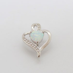 May include: A silver heart-shaped pendant with a white opal gemstone in the center and small clear cubic zirconia stones around the edge.