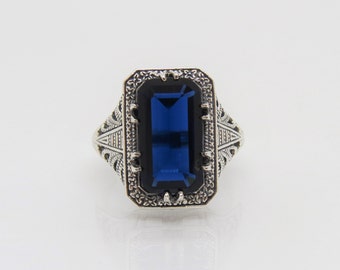 May include: A silver ring with an intricate filigree design and a large, rectangular, dark blue gemstone.