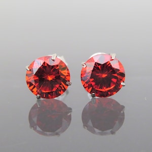 May include: A pair of silver stud earrings with round, bright orange gemstones.