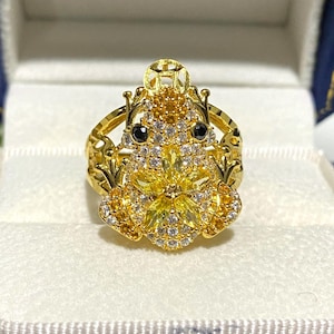 Puede incluir: Un anillo de oro con un diseño de rana detallado con piedras de circonita cúbica amarillas y blancas y acentos negros.