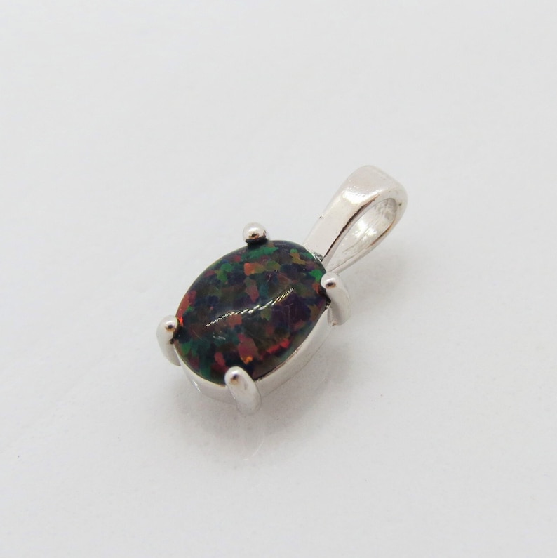 Puede incluir: Un colgante de plata con una piedra preciosa de &oacute;palo negro. El &oacute;palo tiene un fondo oscuro con destellos de verde, rojo y azul.