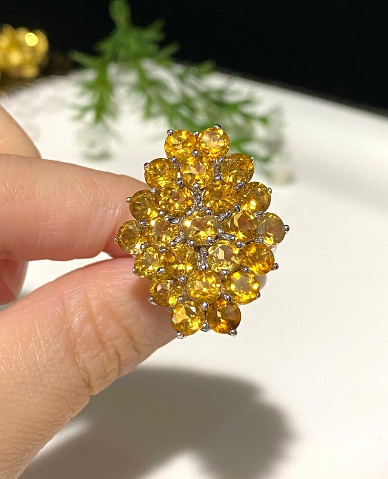 May include: A large, yellow gemstone ring with a cluster of round stones set in silver. The ring is designed in a flower shape.