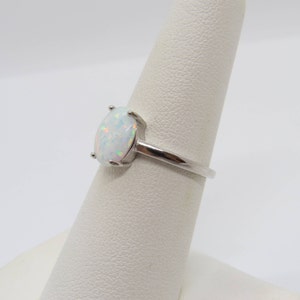 Peut inclure: Une bague en argent avec une opale blanche. La bague est sur un pr&eacute;sentoir blanc.