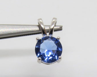 May include: A silver pendant with a round blue gemstone set in a prong setting.