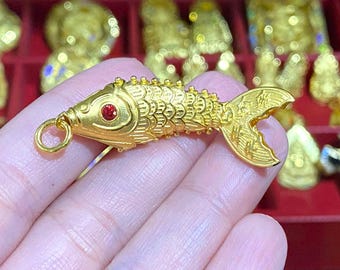 May include: A gold-colored fish charm with a red gemstone eye. The charm has a loop for attaching to a necklace or bracelet.