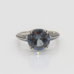 May include: A silver ring with an intricate design on the band and a large, round, blue gemstone in the centre.