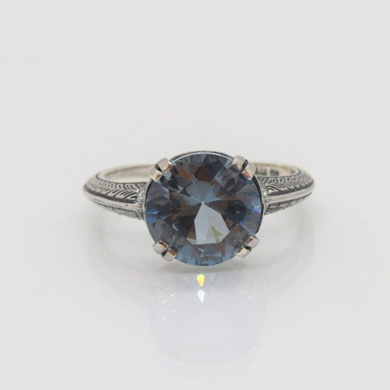 May include: A silver ring with an intricate design on the band and a large, round, blue gemstone in the centre.