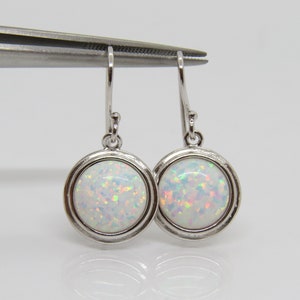 May include: A pair of silver dangle earrings with white opal stones. The earrings have a round shape and a simple design.