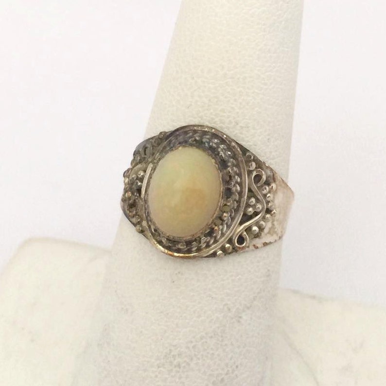 May include: A silver ring with an oval-shaped white opal gemstone set in a filigree design.