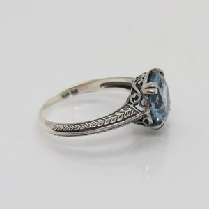 May include: A silver ring featuring an oval blue gemstone set in a filigree design.