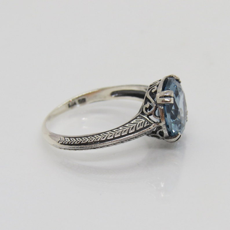 May include: A silver ring featuring an oval blue gemstone set in a filigree design.
