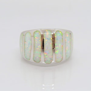 May include: A wide, silver-toned ring with a series of vertical, rectangular opal inlays. The opals display a play of color with flashes of green, blue, and yellow. The ring has a polished finish and a modern design.