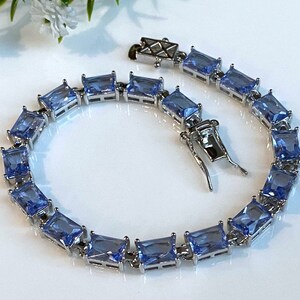 May include: A silver bracelet with light blue square-shaped stones. The bracelet has a clasp closure.