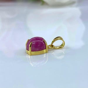 Puede incluir: Un colgante de oro con una piedra preciosa rosa engastada en un engaste de oro. El colgante tiene una simple anilla para sujetarlo a una cadena.