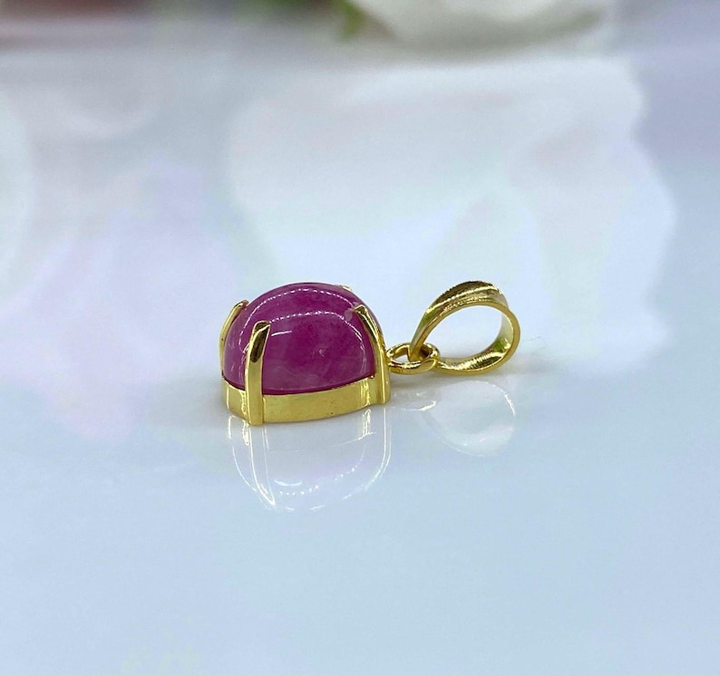 Puede incluir: Un colgante de oro con una piedra preciosa rosa engastada en un engaste de oro. El colgante tiene una simple anilla para sujetarlo a una cadena.