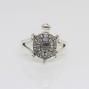 May include: A silver ring with a detailed turtle design. The turtle is facing forward with its head raised and its legs outstretched.