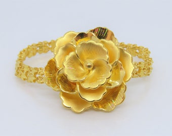 May include: A gold bracelet with a large, ornate rose-shaped charm. The bracelet is made of a delicate chain with intricate details.