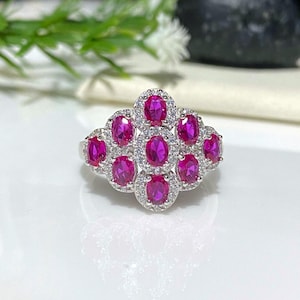 May include: A silver ring with a cluster of pink oval-shaped gemstones surrounded by smaller white gemstones.