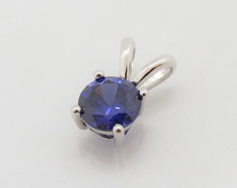 May include: A silver pendant with a round, dark blue gemstone.