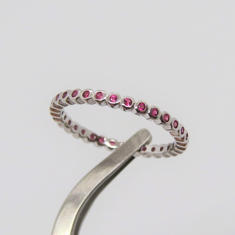 May include: A silver band ring with a row of small pink gemstones.