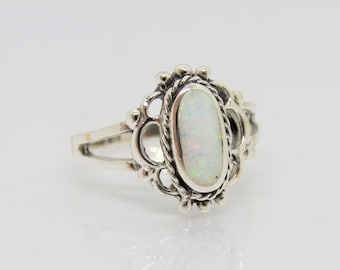Könnte beinhalten: Ein Silberring mit einem ovalen Opal-Edelstein. Der Opal ist in einer dekorativen, filigranartigen Fassung mit geteiltem Schaft gefasst. Der Ring hat eine Vintage-Ästhetik mit einem hellen, irisierenden Opalstein.
