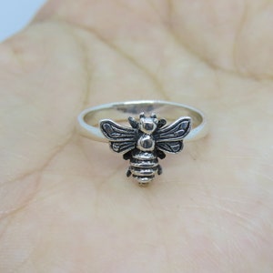 Può includere: Un anello d'argento con un designo di ape dettagliato. L'ape è rivolta in avanti con le ali spiegate.