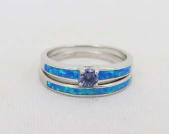 Può includere: Un set di fedi nuziali in argento con un'incisione di opale blu e un'unica pietra preziosa viola al centro.