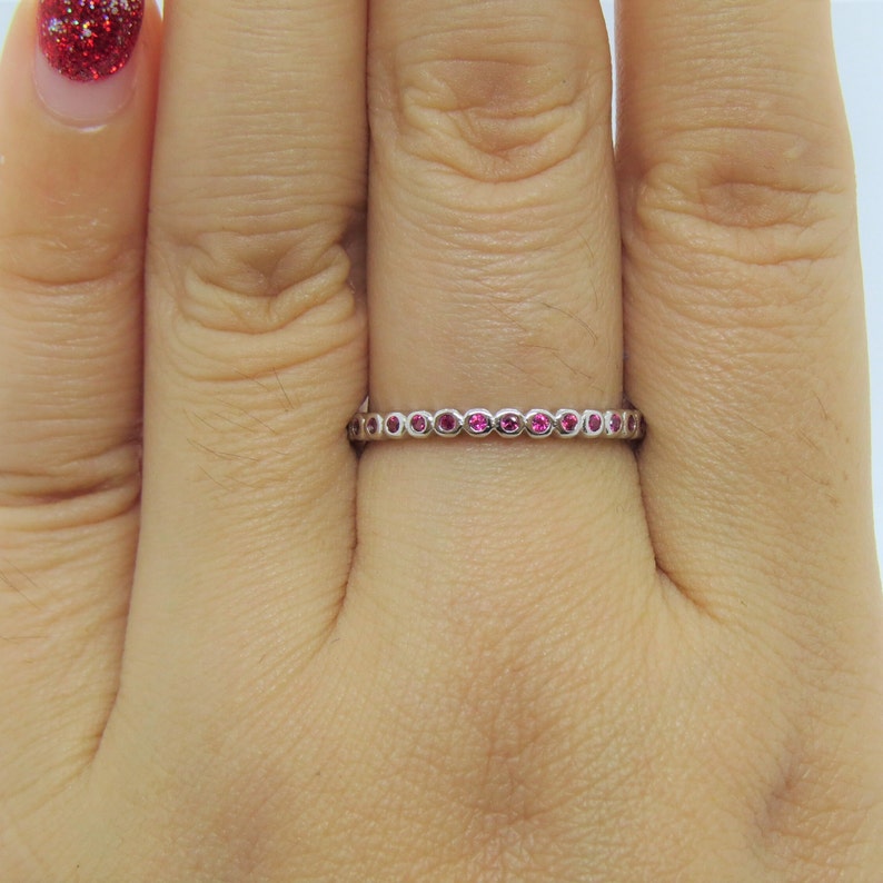 May include: A delicate silver band ring with a row of small pink gemstones.