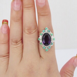 May include: A silver ring with a large oval amethyst gemstone surrounded by smaller green opals.