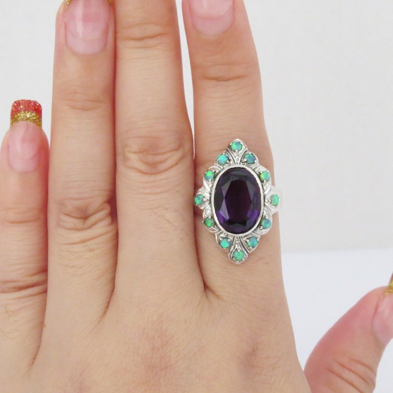 May include: A silver ring with a large oval amethyst gemstone surrounded by smaller green opals.