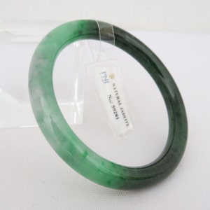 May include: A green jadeite bangle bracelet with a white tag that reads "NATURAL JADEITE No. 5023M".