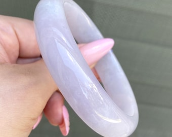 May include: A pale lavender jade bangle bracelet. The bangle is smooth and polished, with a subtle swirl pattern.