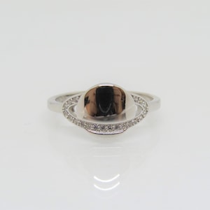 May include: A silver ring with a smooth, oval-shaped center stone surrounded by a halo of small, clear diamonds.