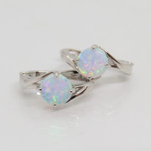 May include: A pair of silver hoop earrings with a white opal gemstone in each. The earrings have a twisted design.