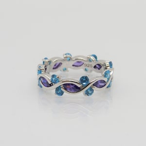 May include: A silver band ring with a design of intertwined blue and purple gemstones. The ring is marked with "925" on the inside.