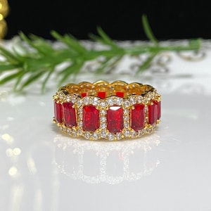 May include: A gold band ring with a row of red rectangular gemstones surrounded by smaller white gemstones.