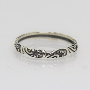 May include: A silver band ring with a delicate, intricate design of swirls and dots.