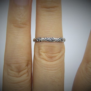 May include: A silver ring with a detailed floral design. The ring is worn on a finger.
