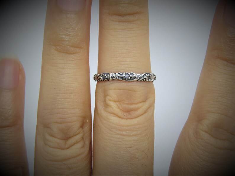 May include: A silver ring with a detailed floral design. The ring is worn on a finger.