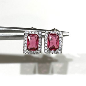 May include: A pair of silver earrings with a pink rectangular gemstone surrounded by a halo of smaller clear gemstones.