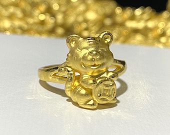 Puede incluir: Un anillo de oro con un tigre de dibujos animados que sostiene un amuleto redondo. El anillo es un diseño chino tradicional.