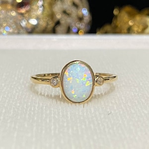 May include: A gold ring with a white opal gemstone and two small diamonds on the band.