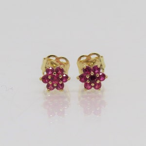 May include: A pair of gold stud earrings with a flower design. Each flower is made of small, red gemstones.