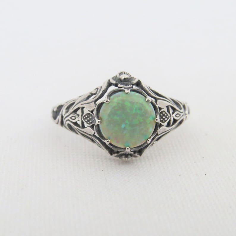 Pode incluir: Um anel de prata com um design ornamentado que apresenta uma pedra de opala verde.
